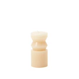 A small, ivory-colored pillar candle with a unique, sculpted design, resembling a totem, on a white background.