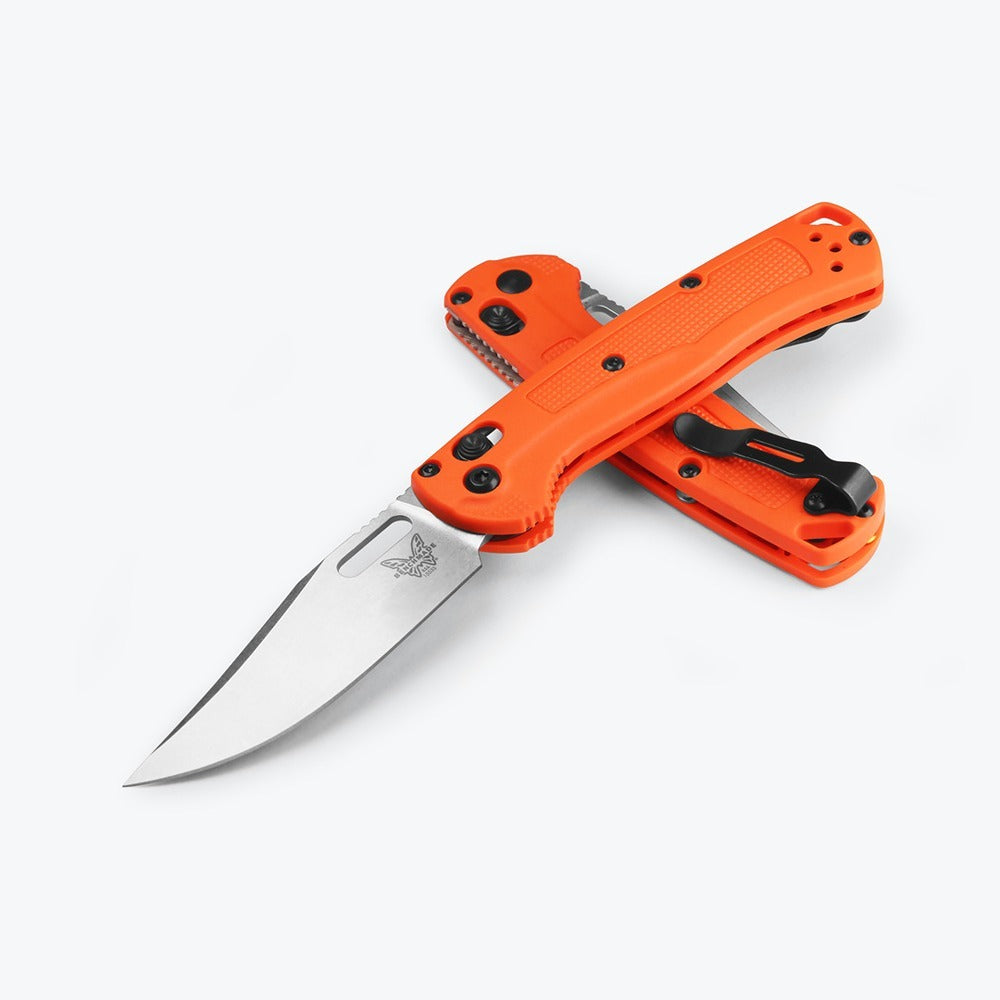 A Benchmade 15533 MINI TAGGED folding knife with an orange Grivory handle and a partially serrated blade, open and displayed against a white background.