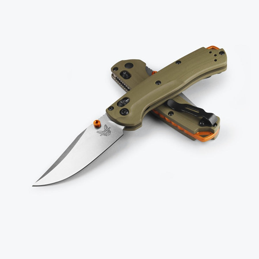 A Benchmade 15534 MINI TAGGEDOUT folding knife with an OD green G10 handle and an orange anodised thumb stud and barrel spacers, featuring a clip point blade.