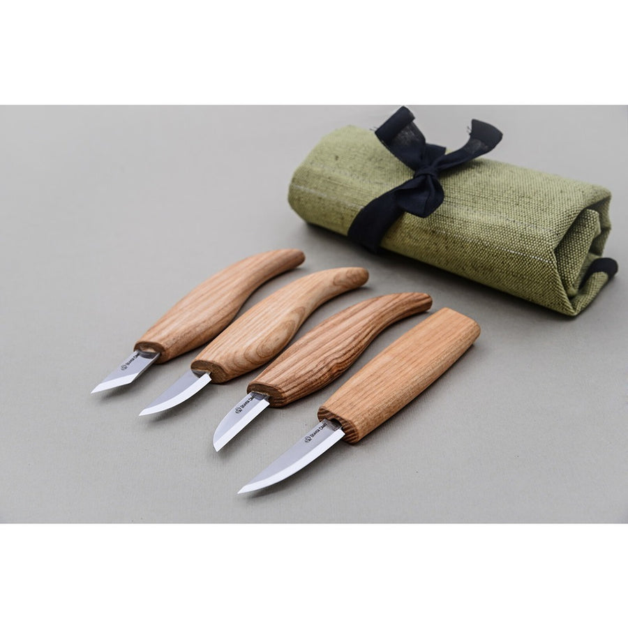 A set of four wooden-handled carving knives with blades, placed in front of a roll of green fabric with a dark blue ribbon. Beaver Craft | King of Knives e-store