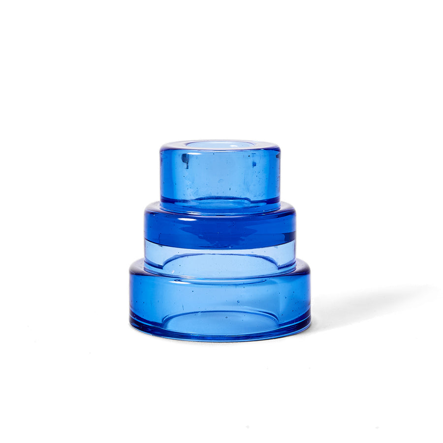 A blue glass candle holder with a tiered design, resembling terraced hillsides, intended for holding taper or tea light candles.